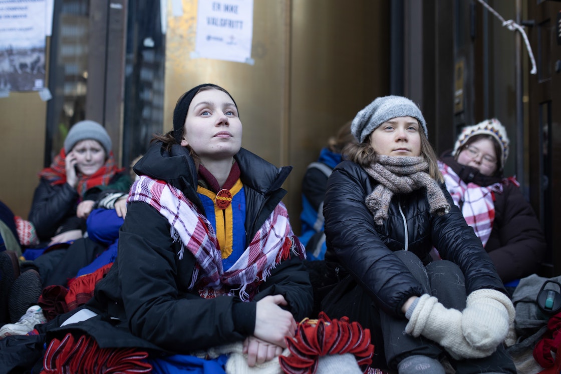 Kvinner sitter på bakken, flere med samisk skjerf og kofte
