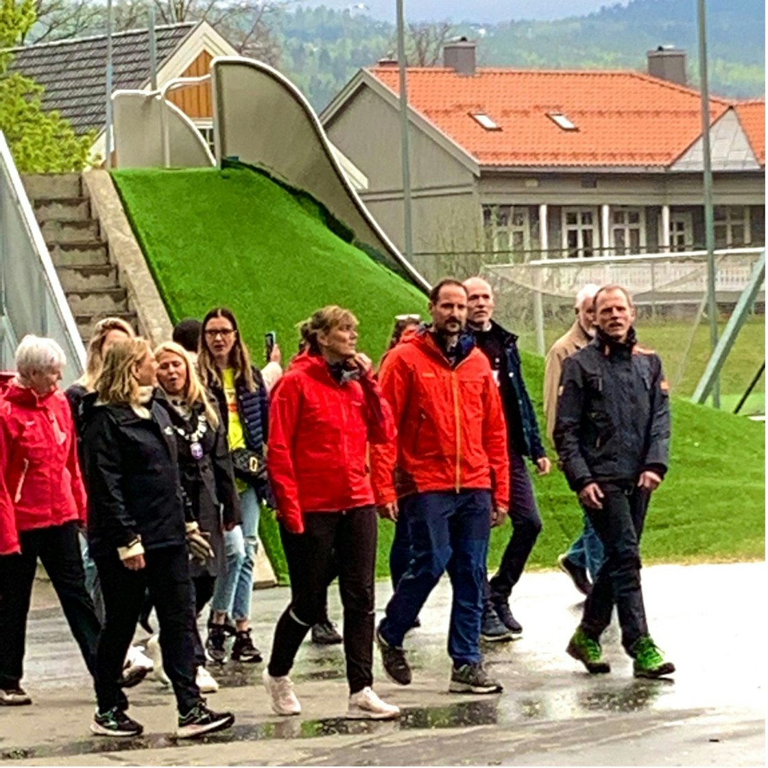 Kronprins Haakon i turklær går sammen med en  gruppe turkledde mennesker på en regnvåt asfaltert vei