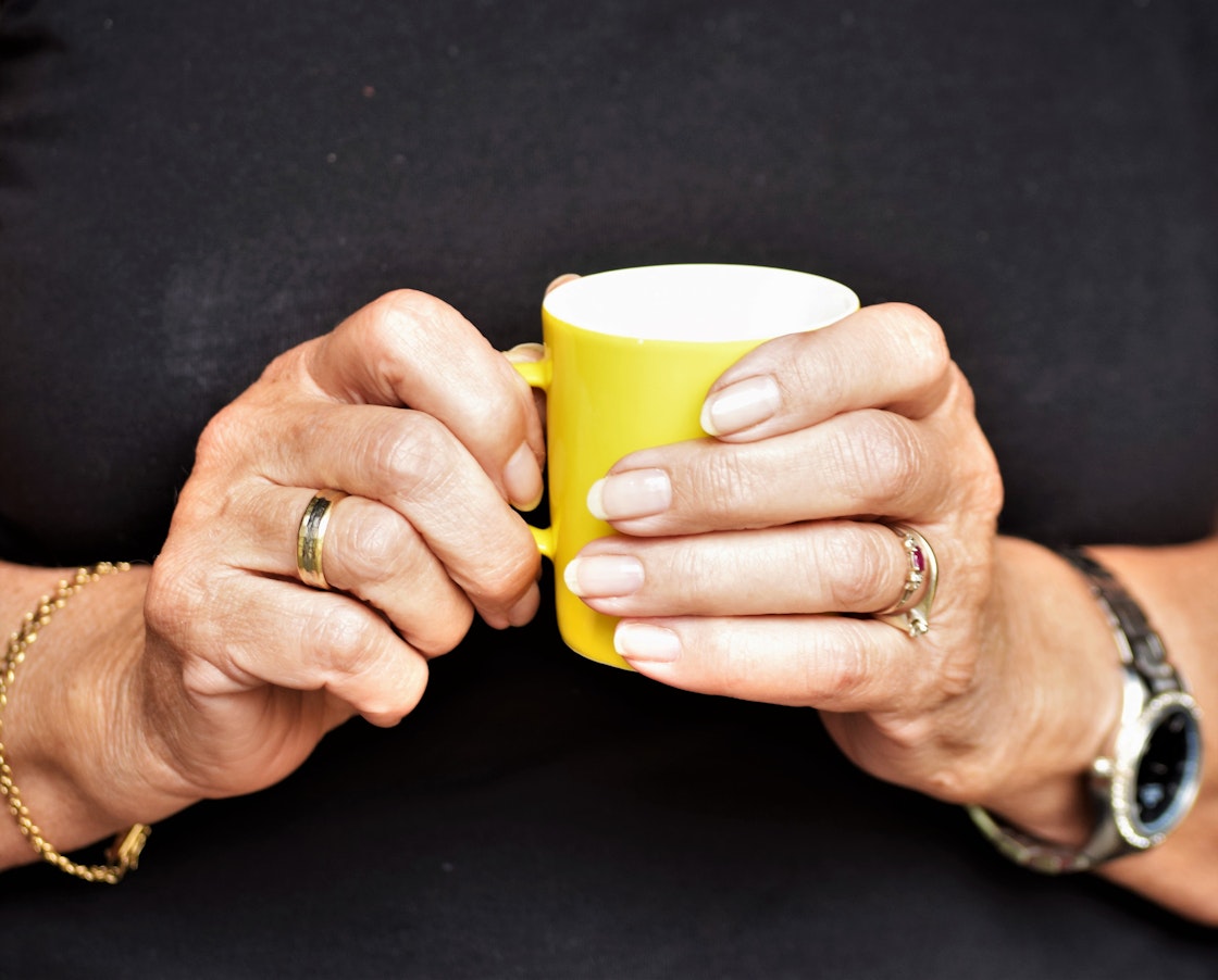 To hender som holder i en gul kopp
