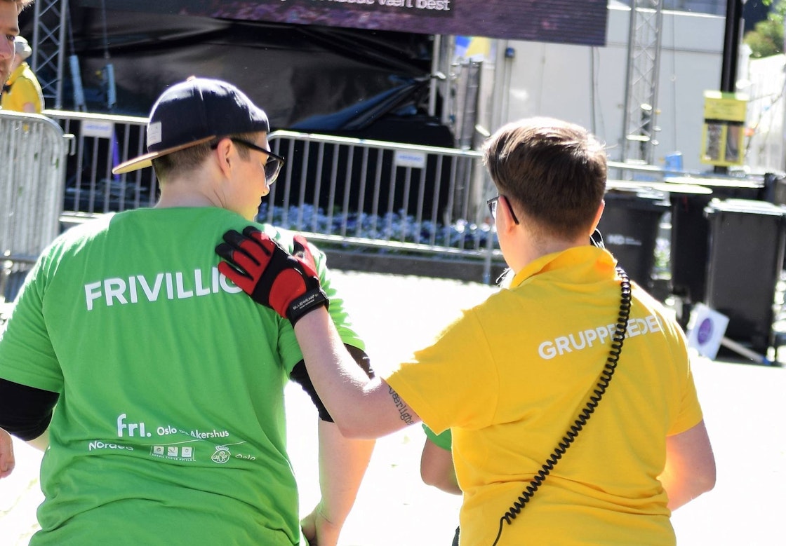 To frivillige med grønn og gul t-skjorte der en av dem holder på skulderen til den andre
