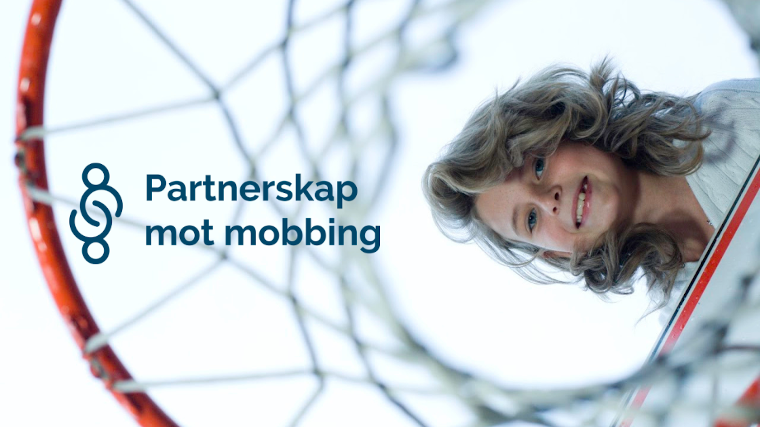 En ung jente ser inn i kameraet og smiler. Tatt fra undersiden og man kan skimte en basketkurv bak.