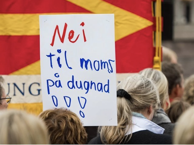Bildet viser en gruppe mennesker som står med en plakat som sier: Nei til moms på dugnad.