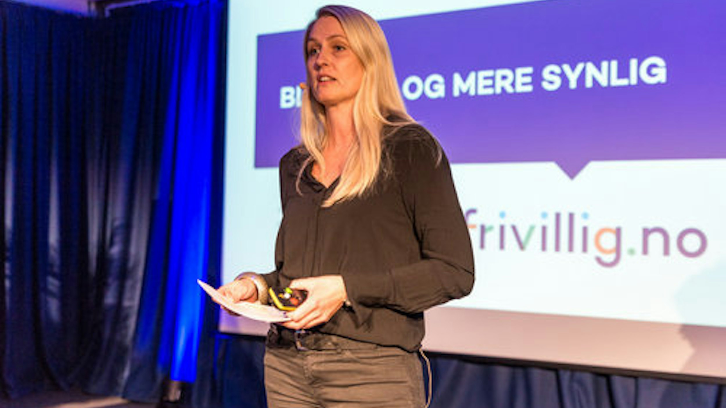 Kvinne som holder presentasjon foran en skjerm med bilde av logoen Frivillig.no