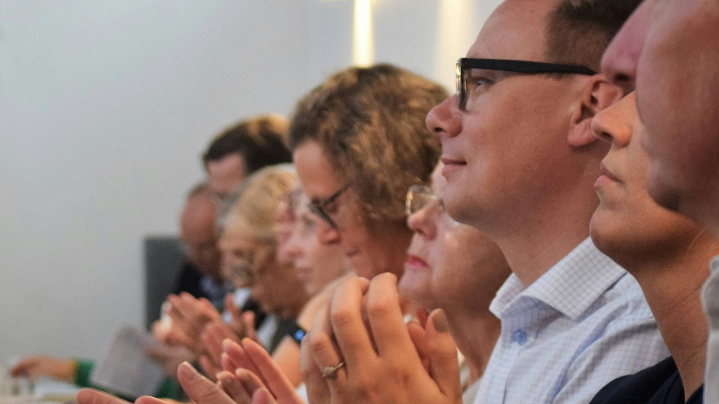 En rad sittende mennesker som appladserer i et møterom.
