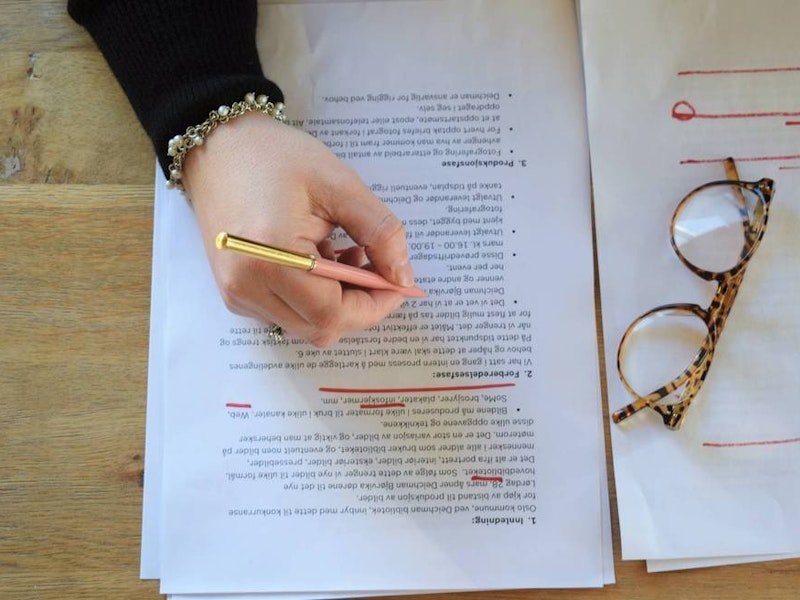En håns skriver notater på et utprintet dokument. Et par briller hviler oppå dokumentet.