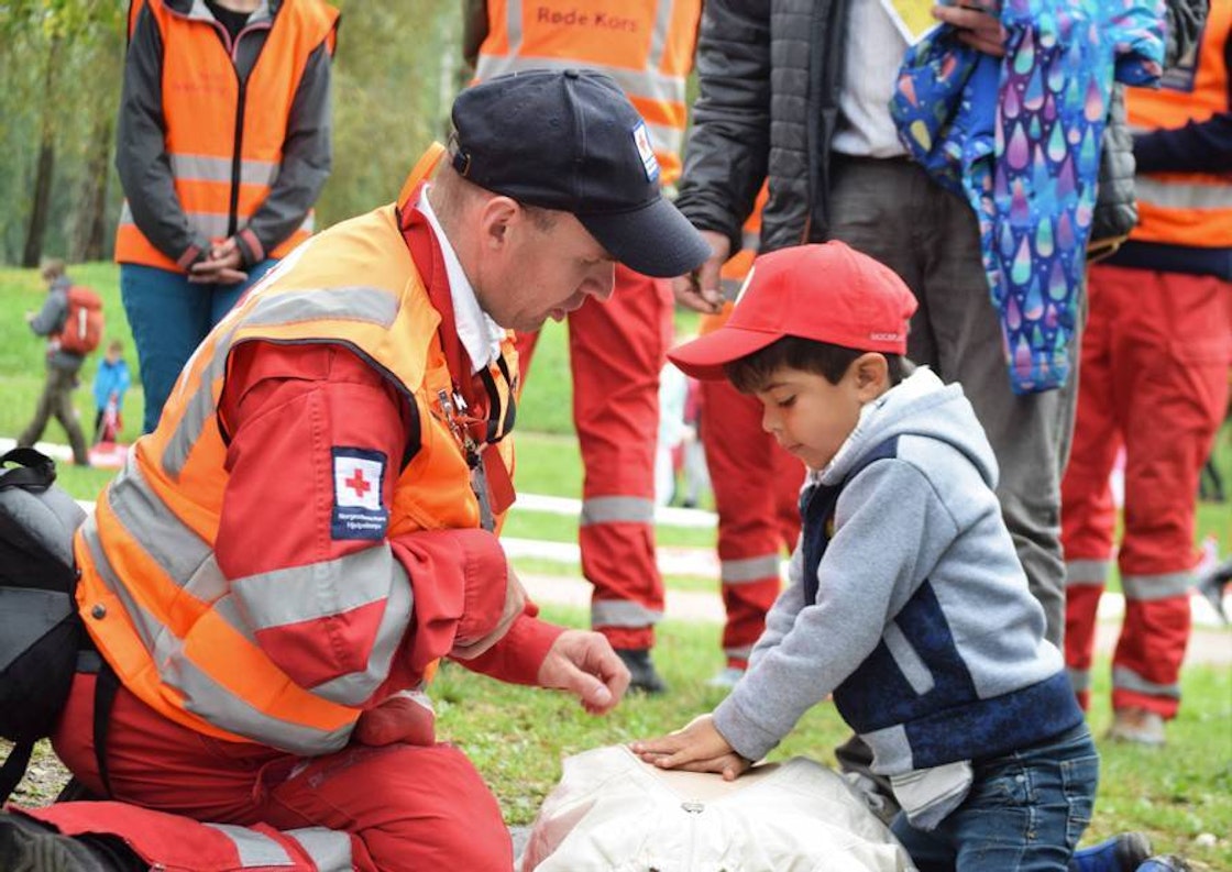 En voksen mann med Røde Kors-uniform viser et gutt hjertekompressjoner.